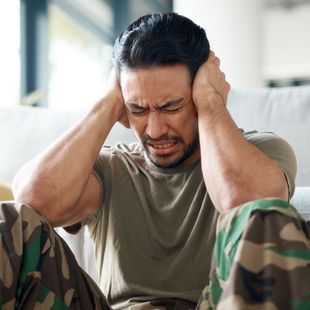 a man sitting on a couch covering his ears with his hands