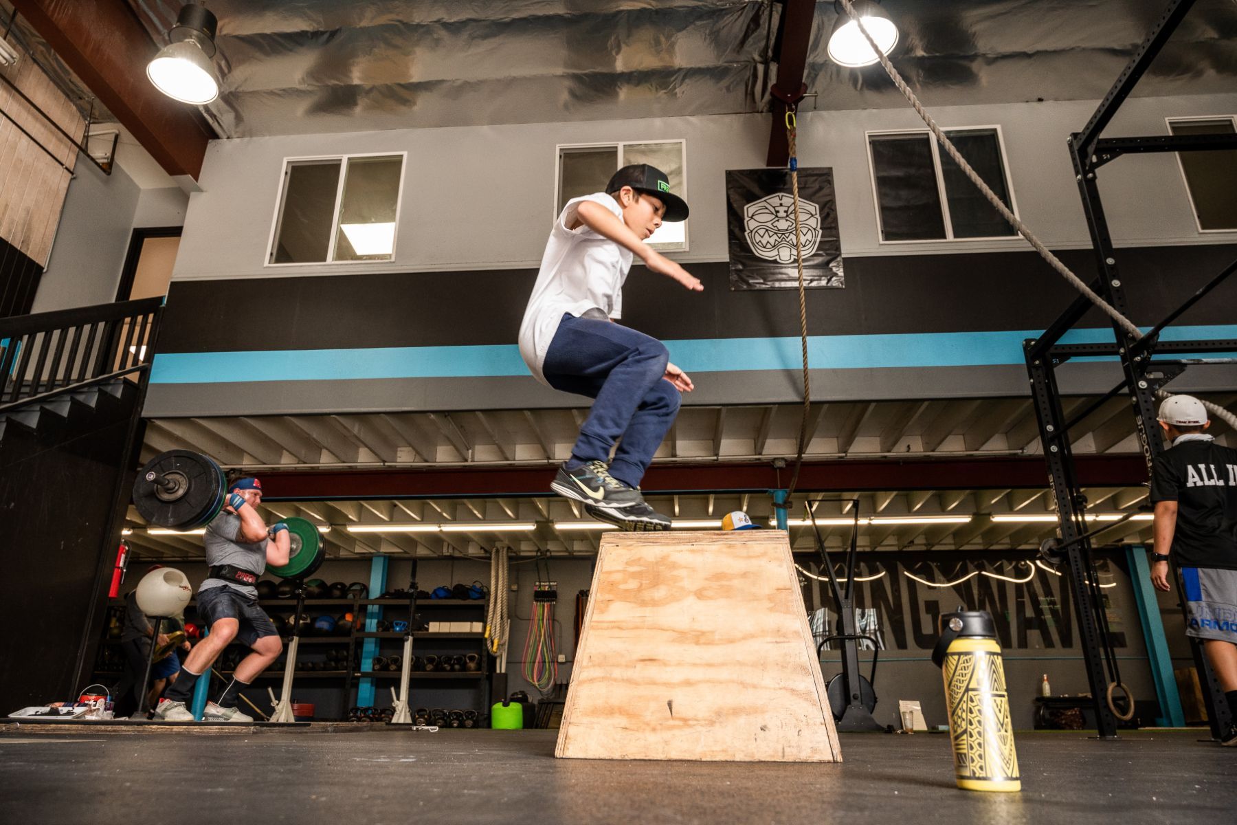 A man is jumping over a wooden box in a gym.