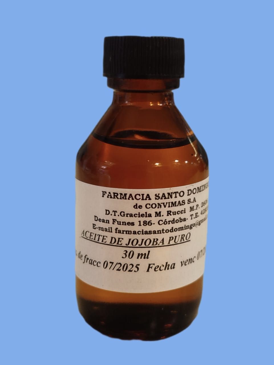 Pequeña botella de vidrio ámbar etiquetada "Aceite de Jojoba Puro" (aceite de jojoba puro) con tapa negra, sobre fondo azul.