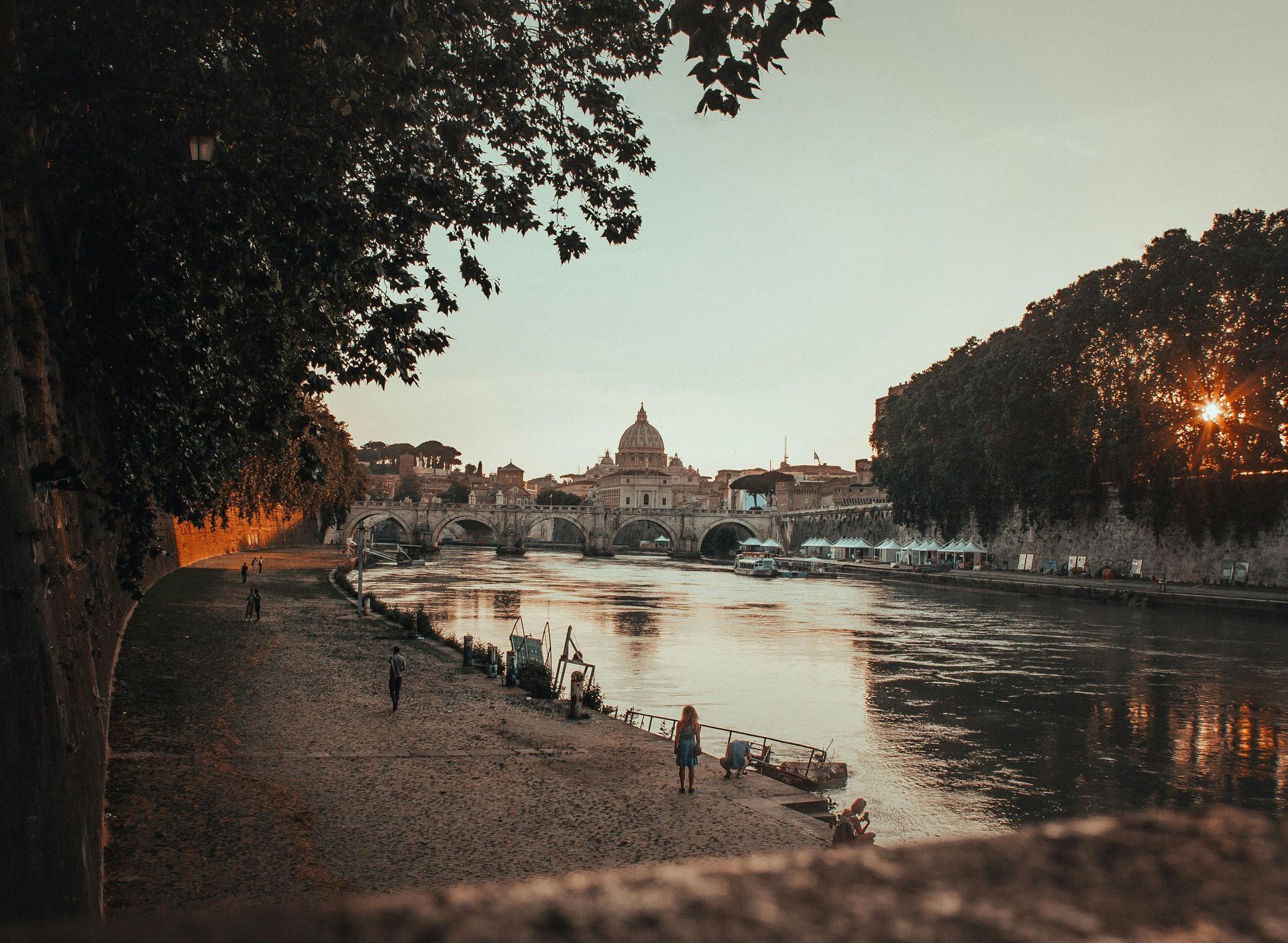 A river with a bridge in the background and people walking on the shore