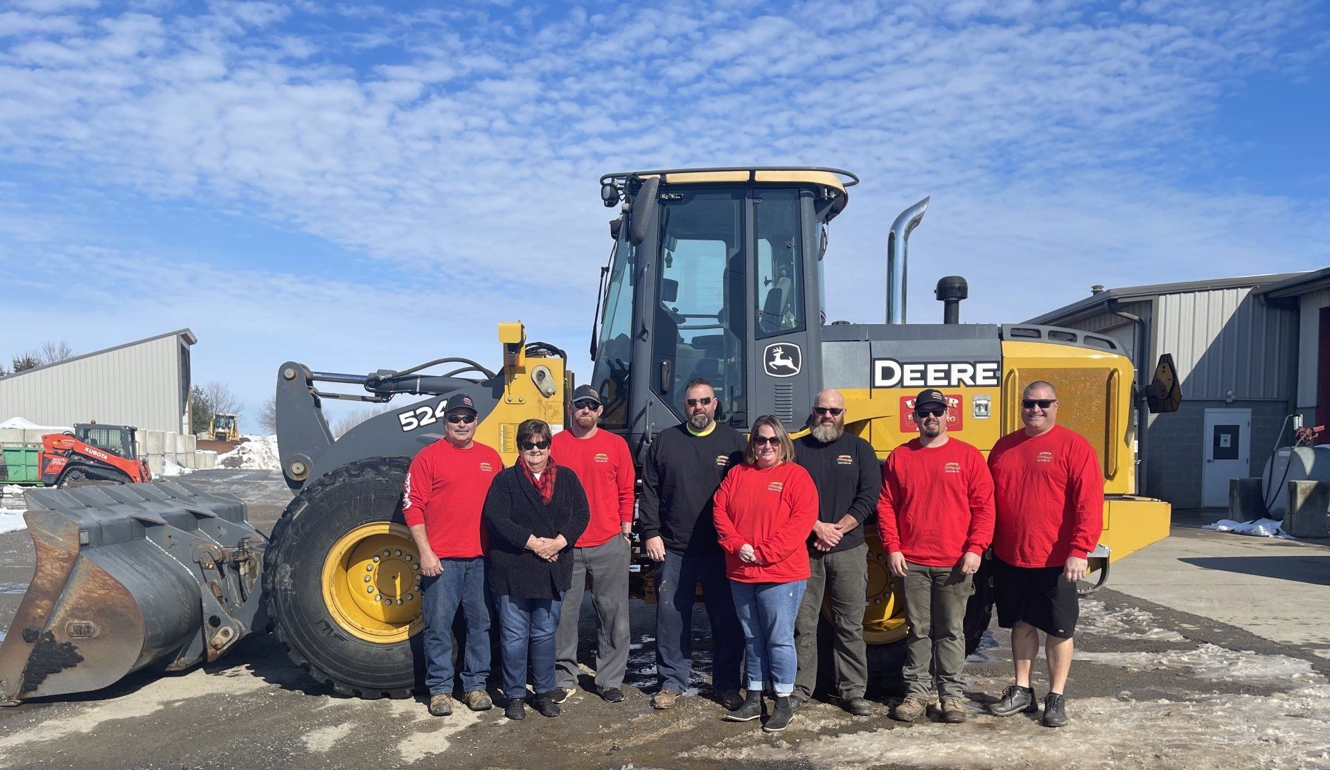 A group of people are posing for a picture in front of a deere tractor.