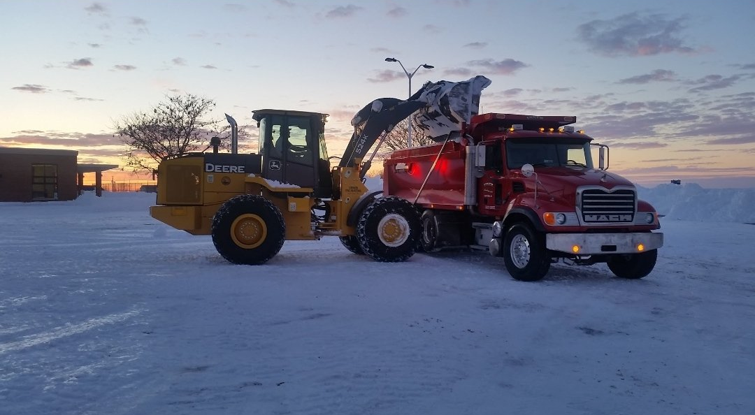 A bulldozer is being towed by a red truck in the snow.