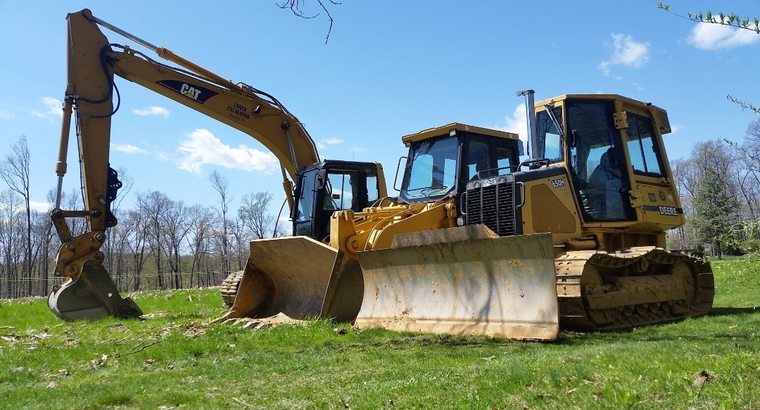 A bulldozer and an excavator are parked in a grassy field.