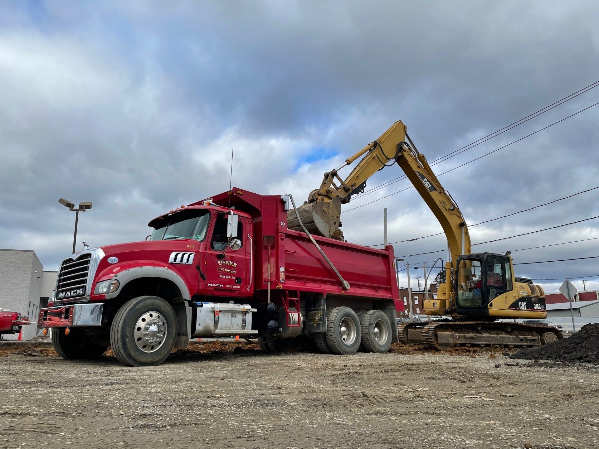 A red dump truck is parked next to a yellow excavator.