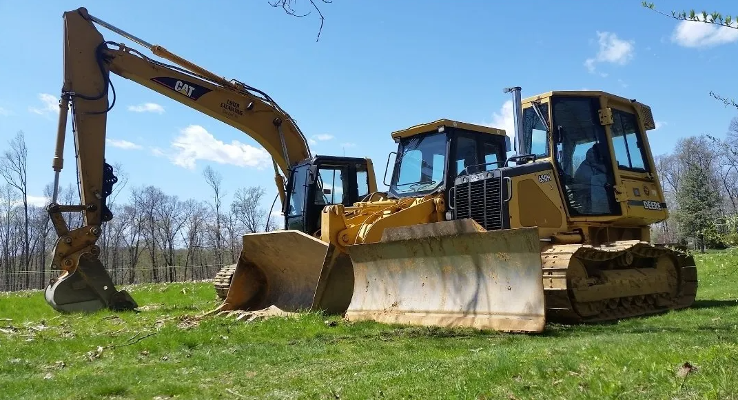 A bulldozer and an excavator are parked in a grassy field.