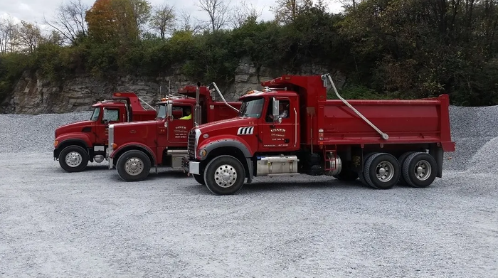Three red dump trucks are parked in a gravel lot.