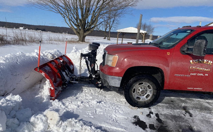 A red truck with a snow plow attached to it is parked in the snow.