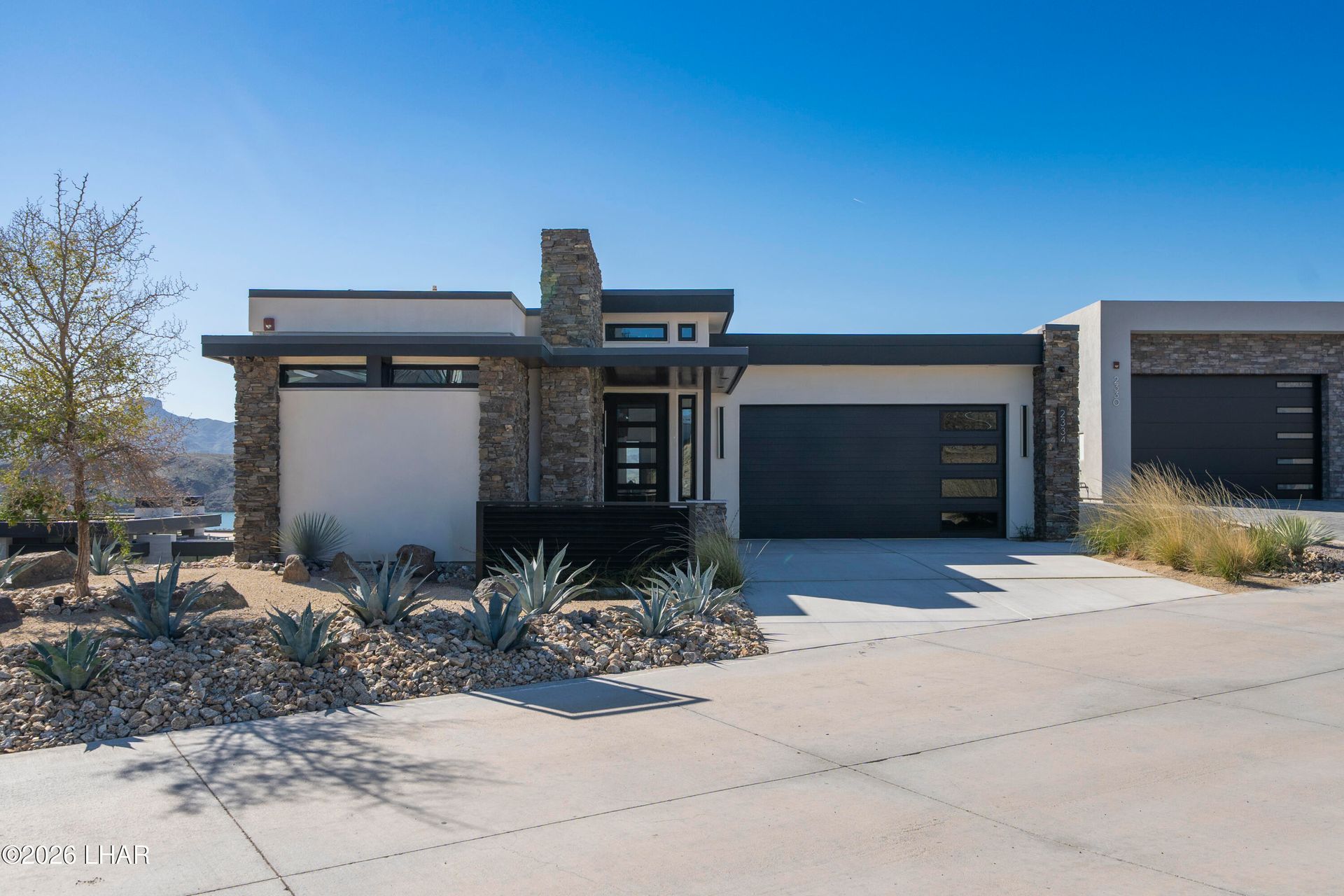 Modern single-story house with stone accents, garage, and desert landscaping under a clear blue sky