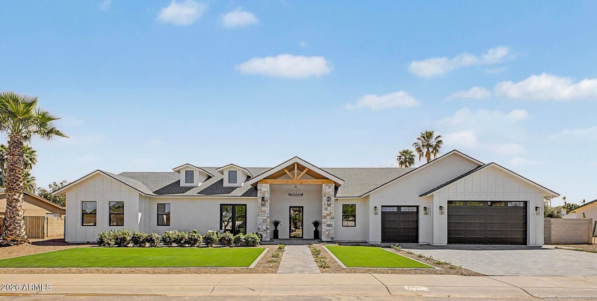 Wide white suburban house with a front lawn, stone walkway, and double garage under a blue sky