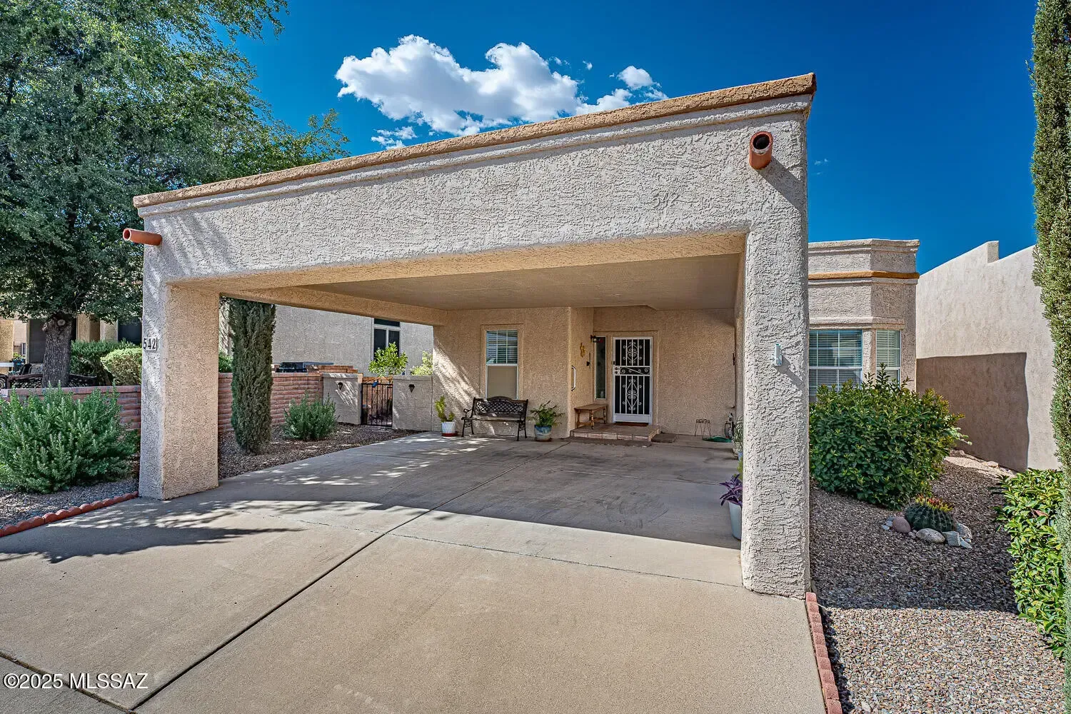 Covered driveway of a beige brick house with a two-car carport and desert landscaping