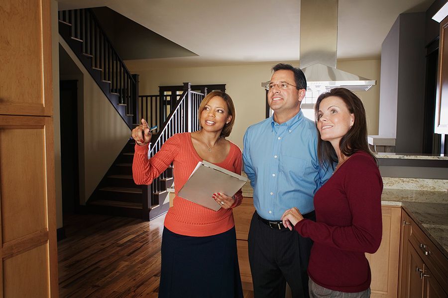 Three people smiling and pointing at a model kitchen in a home interior.