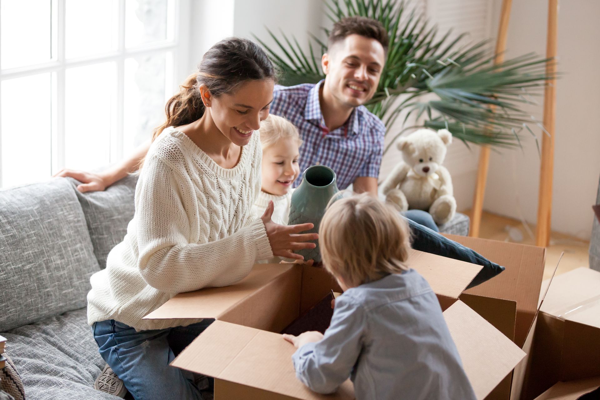 Family unpacking boxes in a bright living room, with a dog watching nearby.