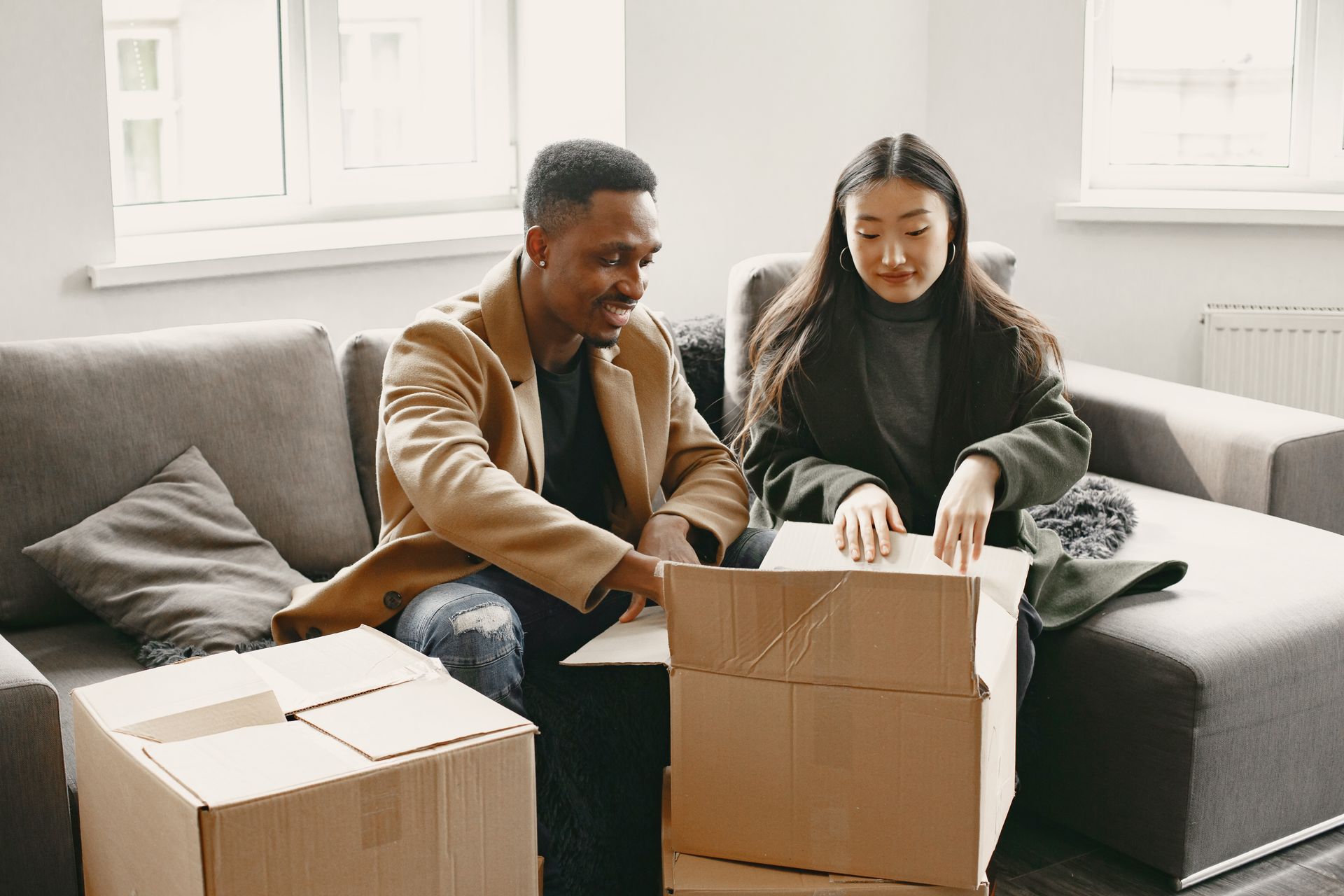 Two people unpacking cardboard boxes on a couch in a bright living room