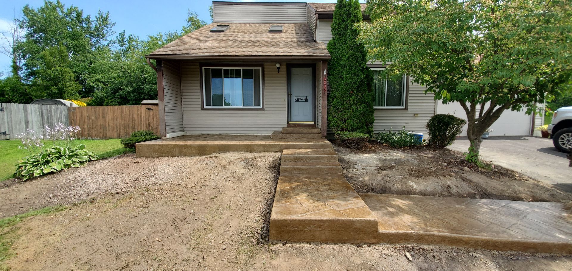 A small house with concrete steps leading to the front door, surrounded by dirt and a tree.