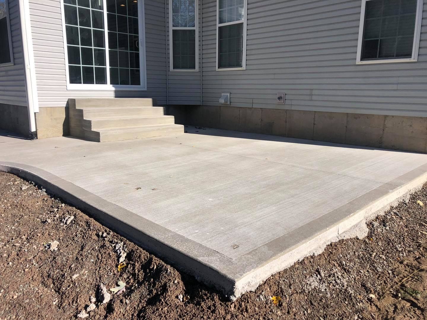 Concrete patio with steps leading to a sliding glass door, next to a house with light siding.