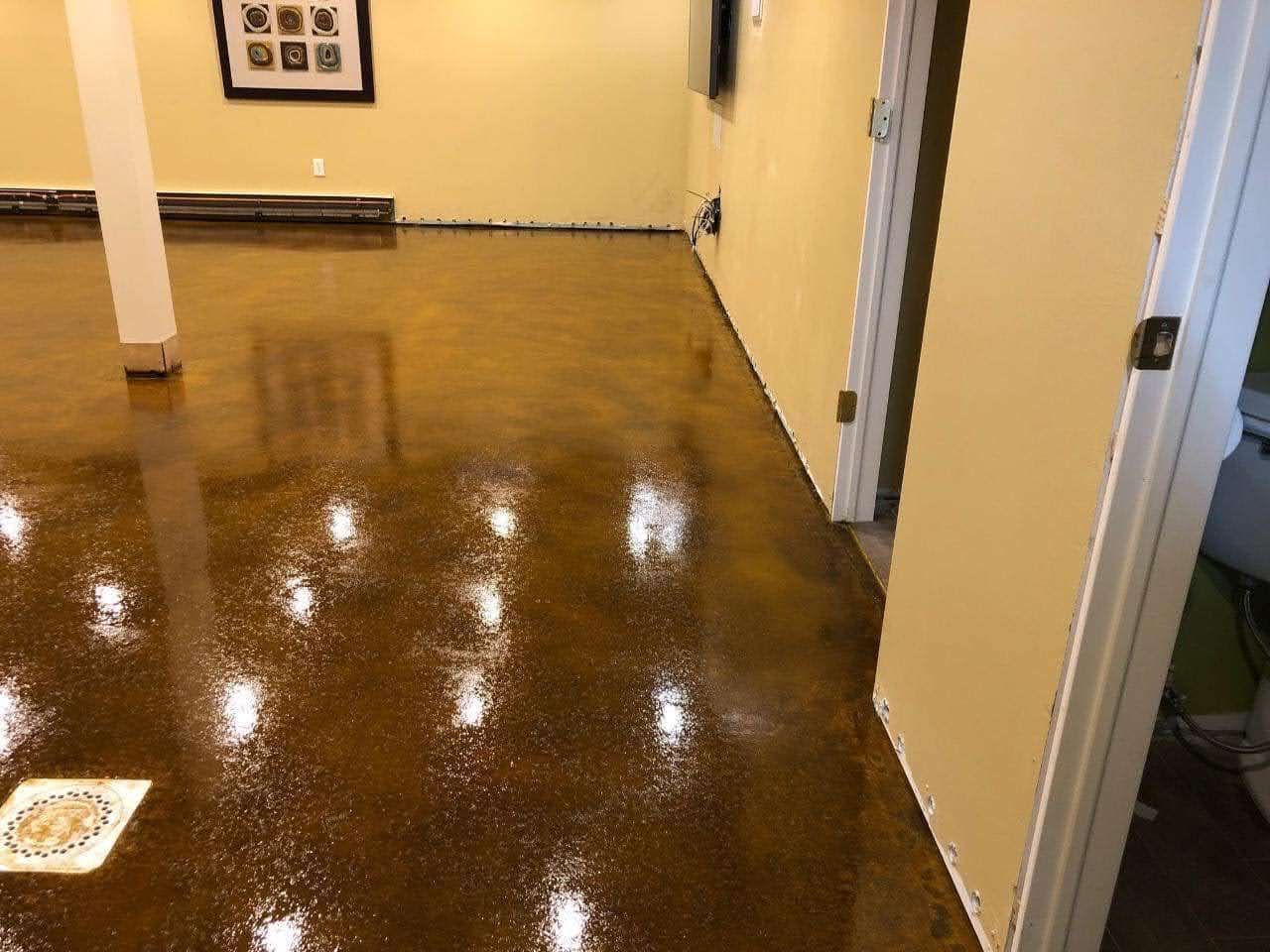 A shiny, brown epoxy floor in a room with beige walls. A white column and a partially open door are visible.