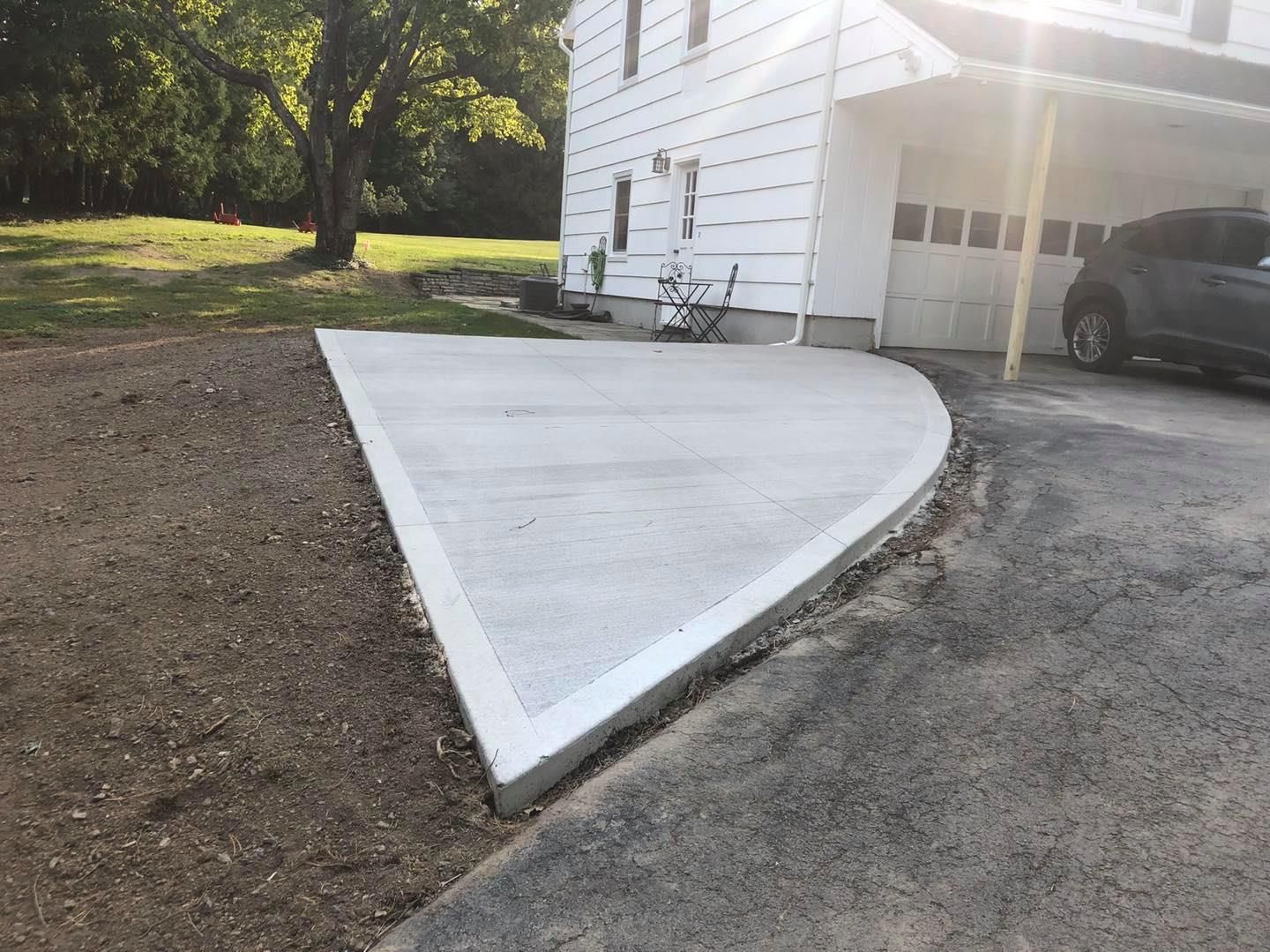 Newly poured concrete driveway section next to a white house with a parked car.