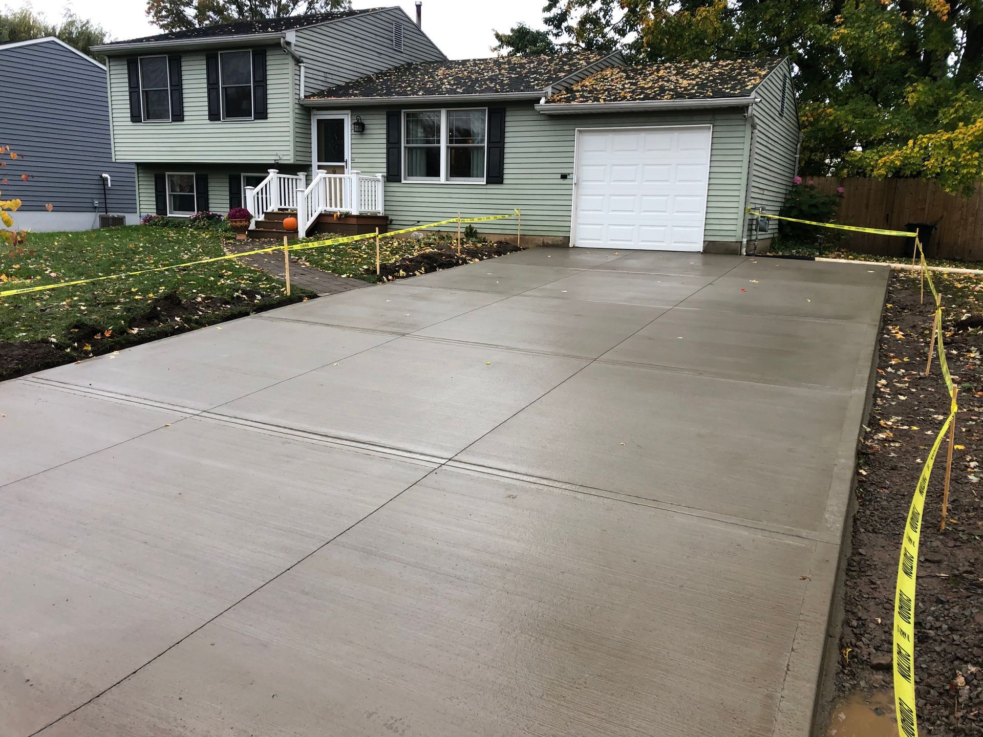 New concrete driveway in front of a house; wet and gray with caution tape around the edges.