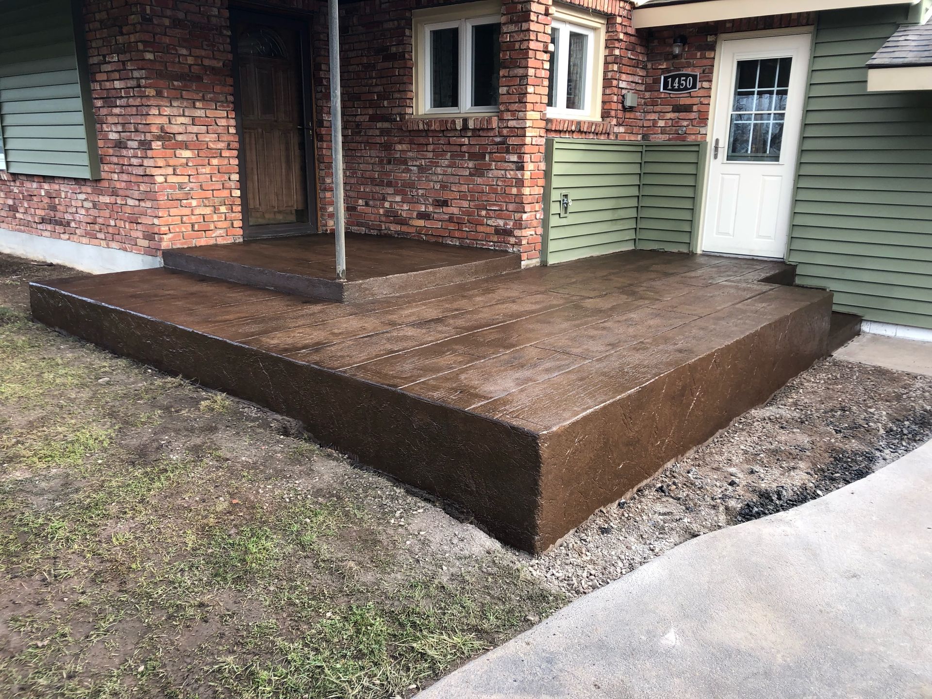 Brown concrete porch and steps in front of a brick and green house with a white door.
