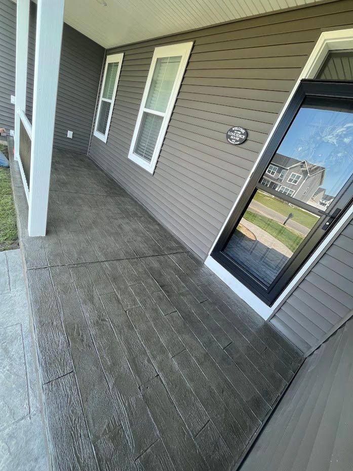 Gray front porch with simulated wood grain concrete. House has gray siding, two windows, and a glass door.