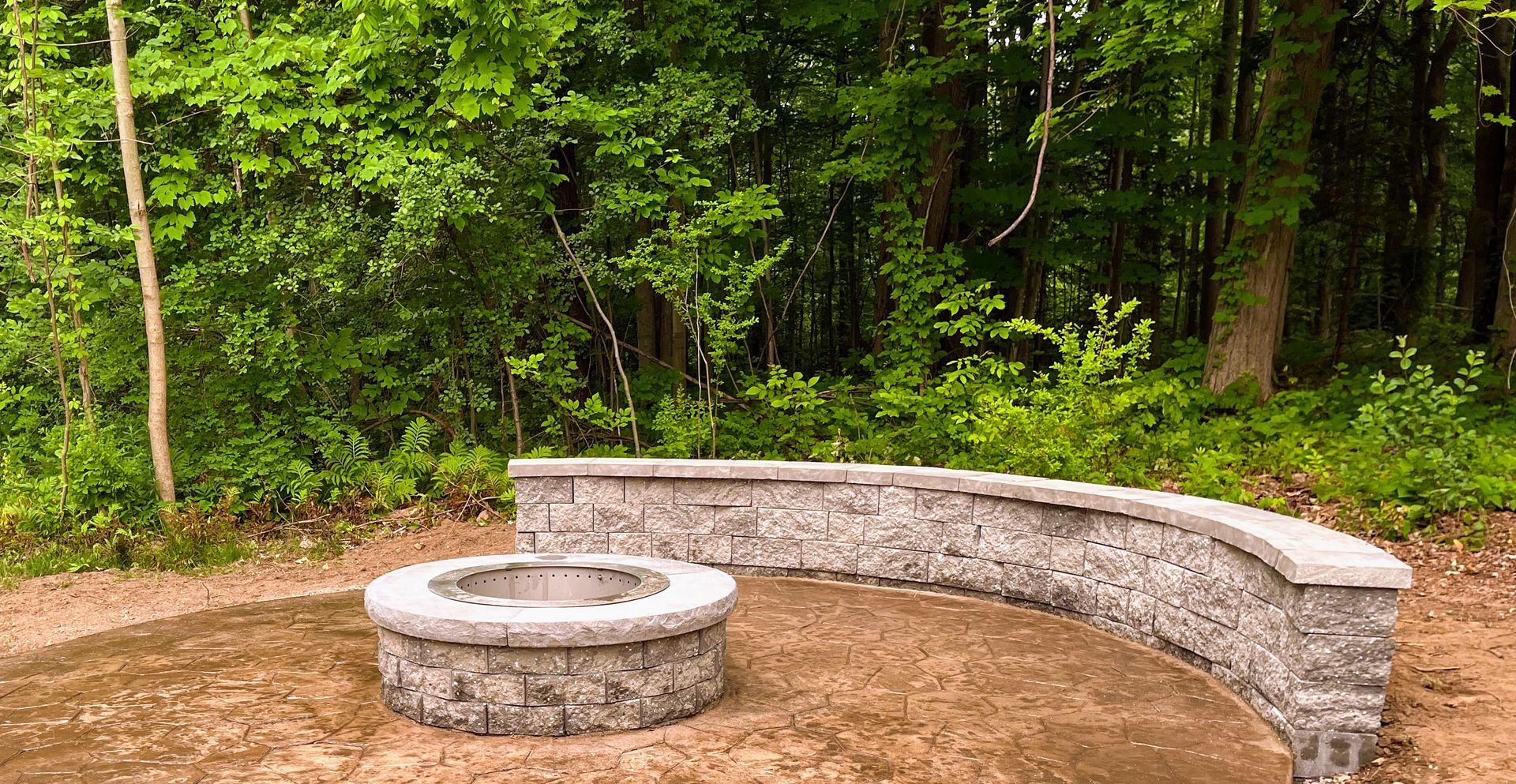 Stone fire pit and curved bench in a wooded area.
