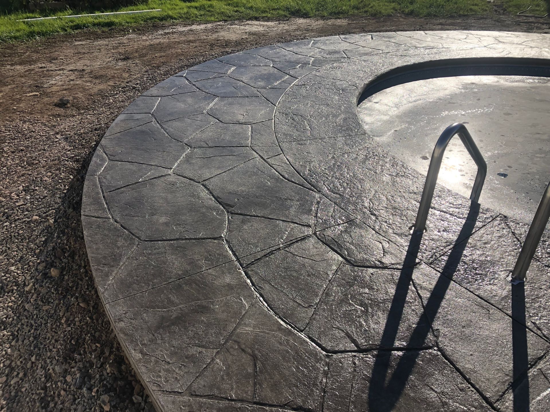 Gray stamped concrete with a stone pattern, curved shape, and part of metal object in the foreground.