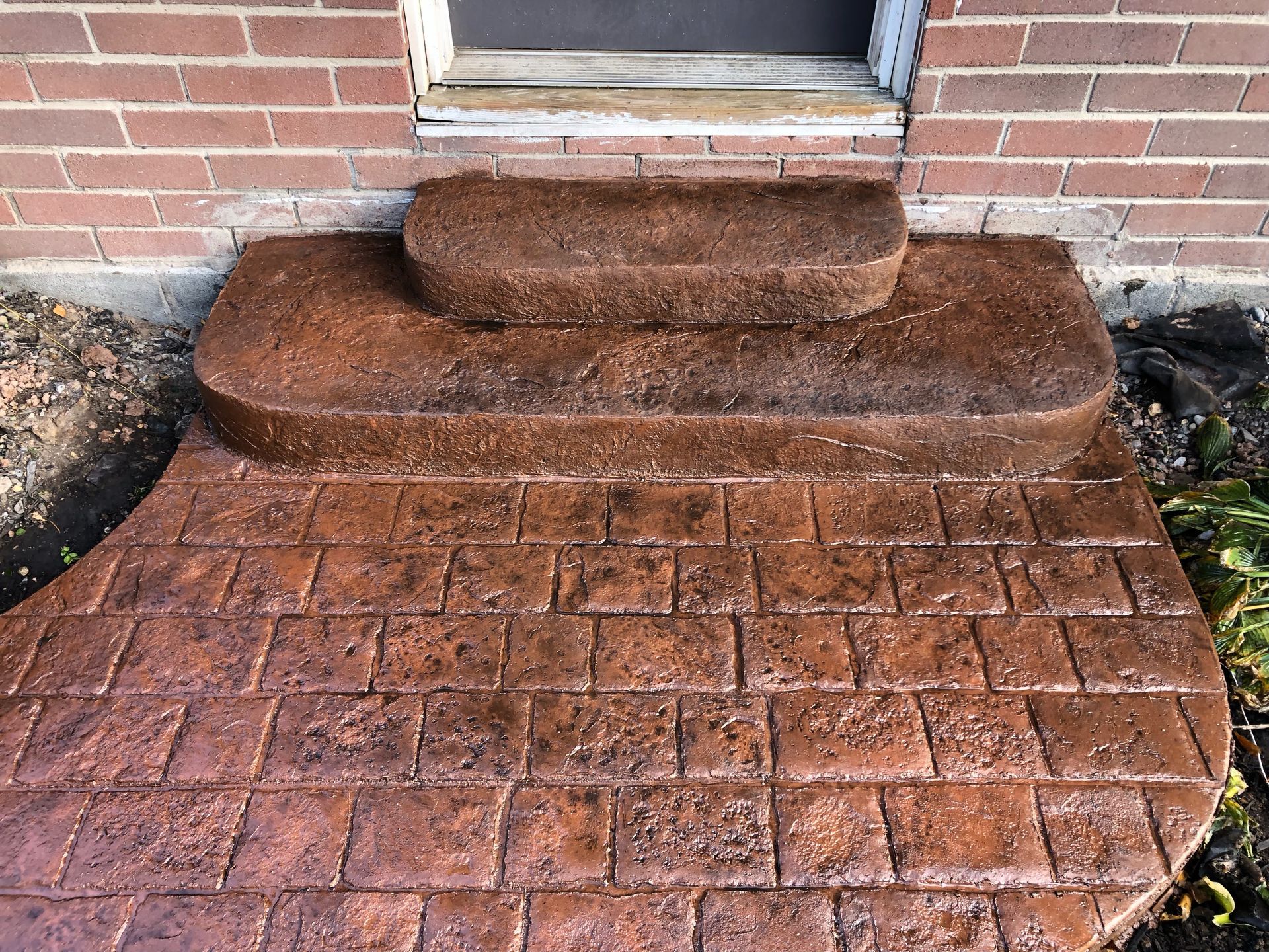 Brick-patterned concrete steps leading to a doorway; brown hue.