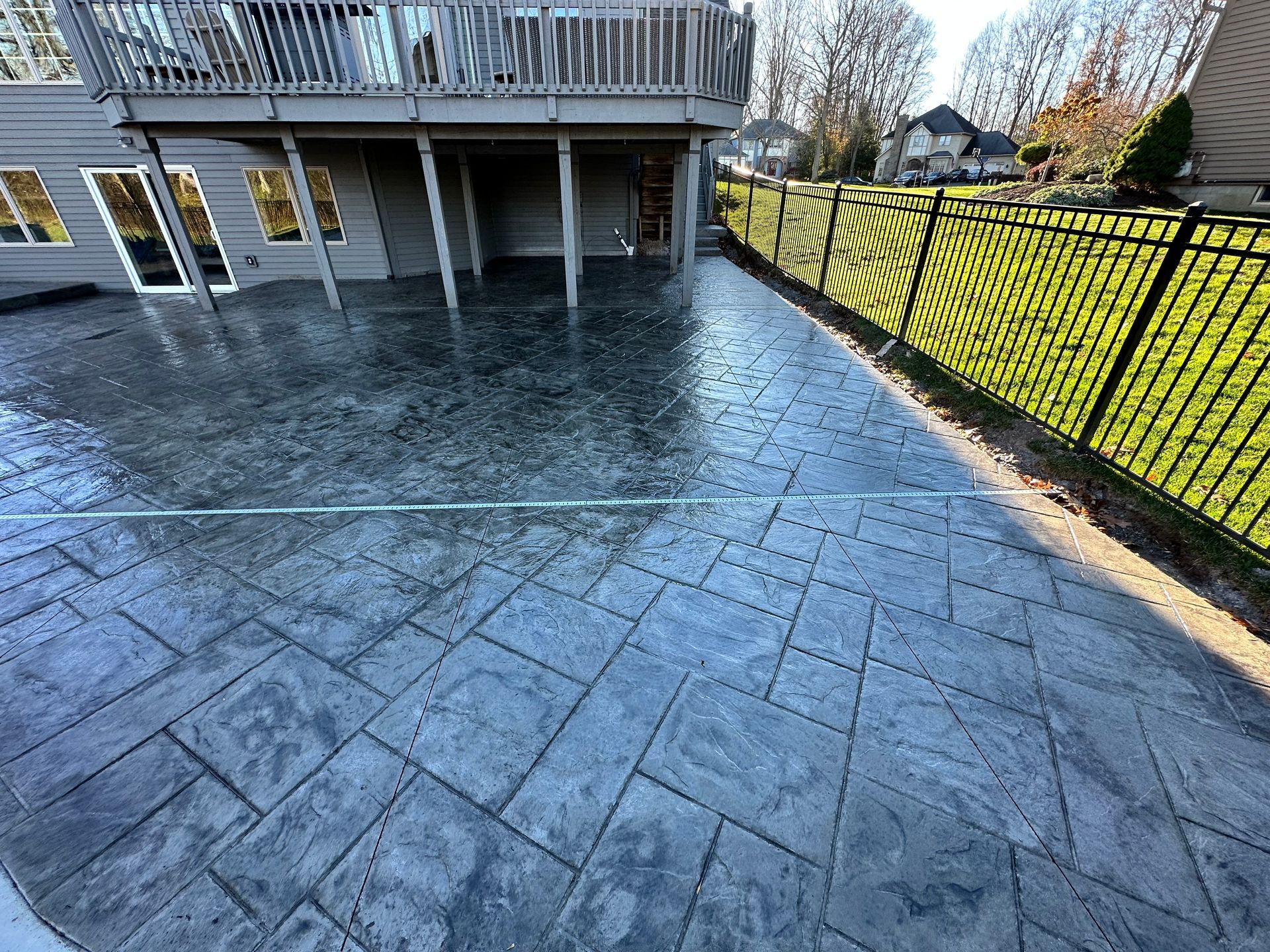 Gray stamped concrete patio with a house and black fence in the background.