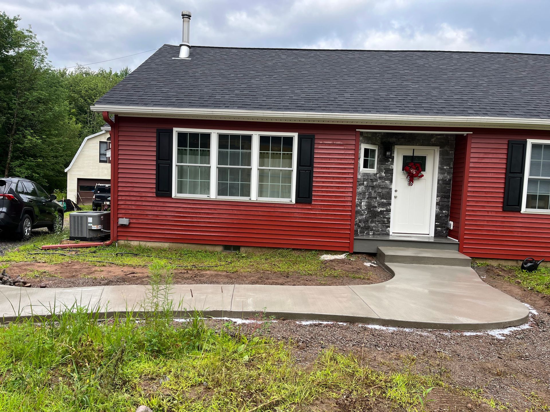 Red house with white trim, black shutters, and a concrete path leading to the front door.