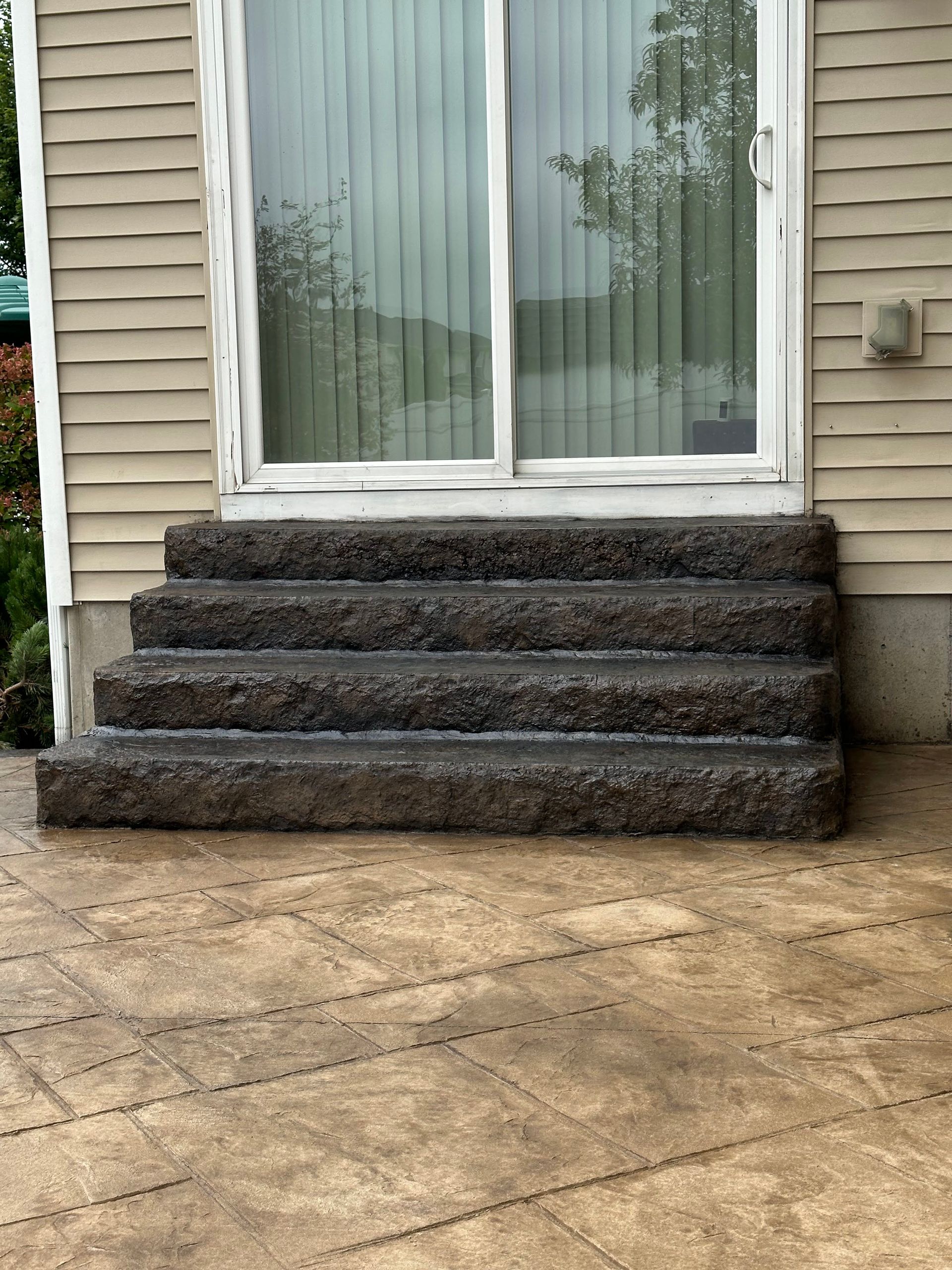 Concrete steps leading to a sliding glass door, set against beige siding.