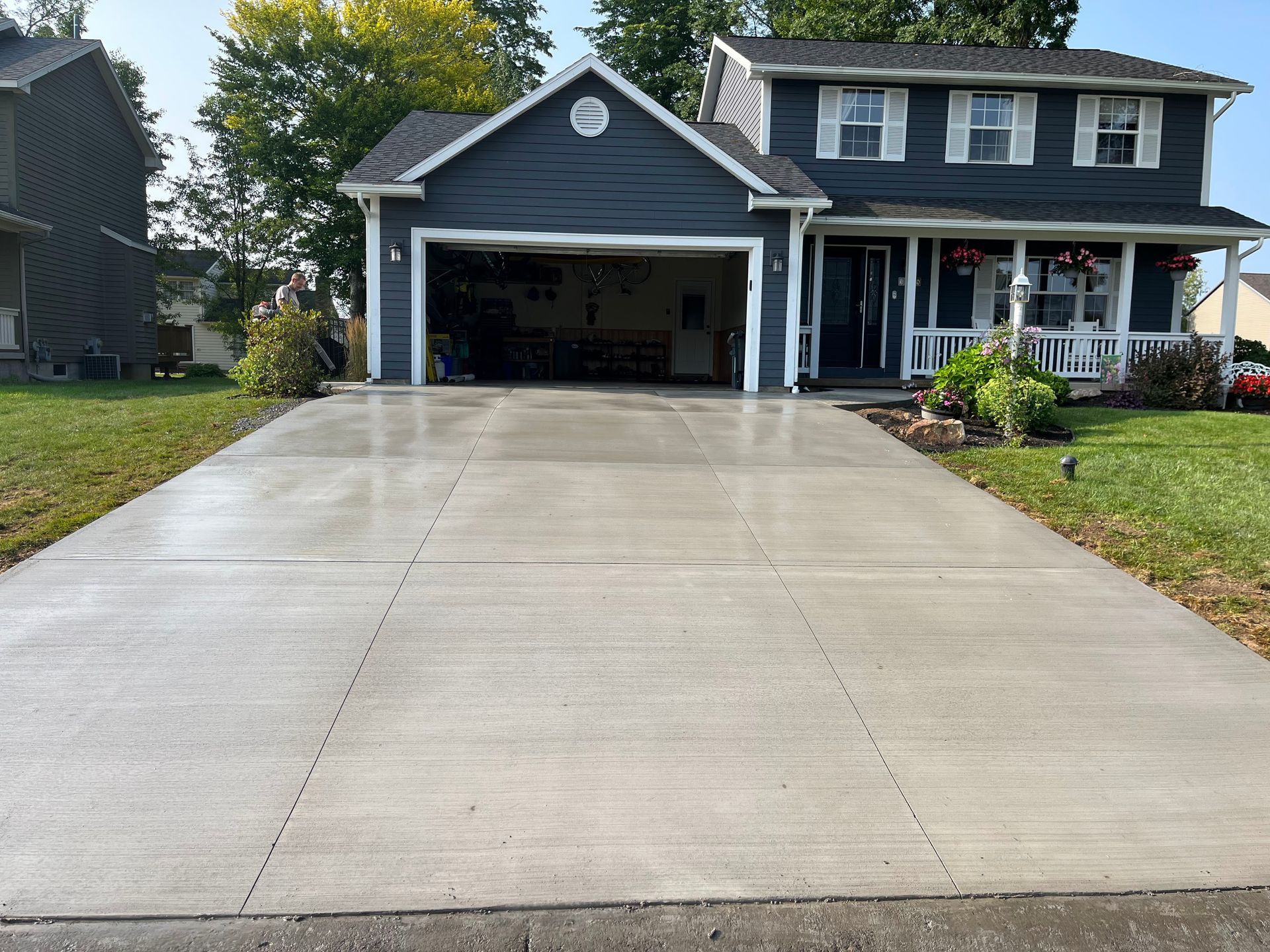Gray concrete driveway leading to a blue two-story house with an open garage.