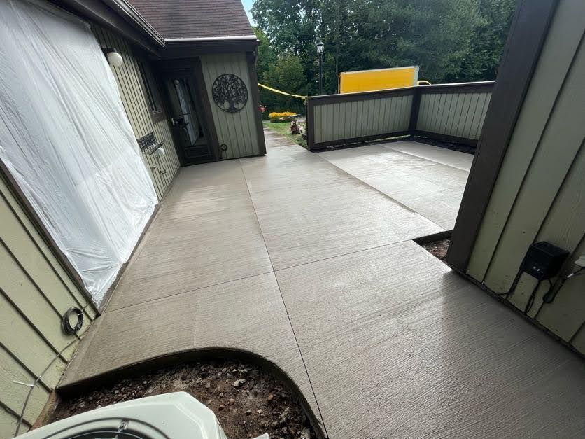 Concrete patio beside a house with a decorative door, a/c unit, and fenced deck.