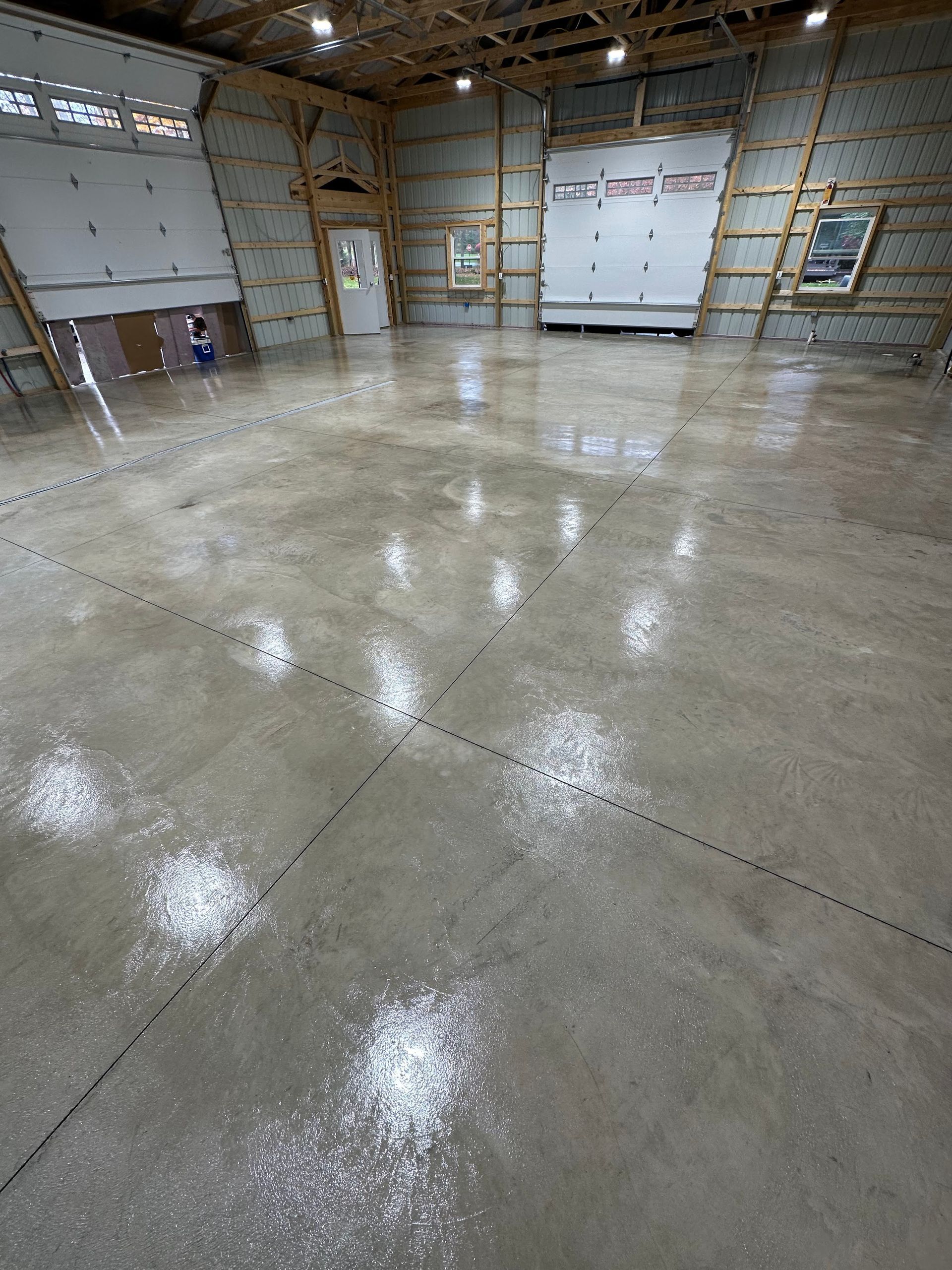 Empty industrial warehouse with polished concrete floor, garage doors, and open ceiling.