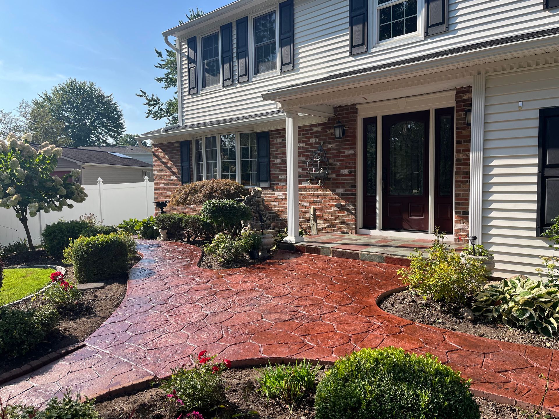 A red brick-patterned walkway leading to a white two-story house with black shutters and a red door.