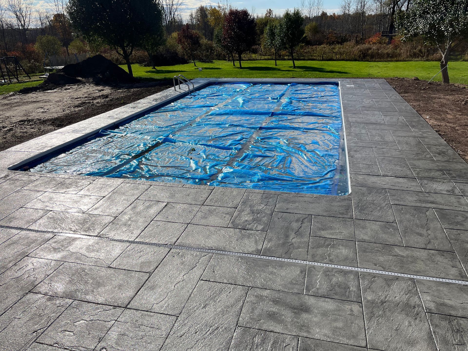Rectangular pool covered in blue tarp, surrounded by gray concrete patio.