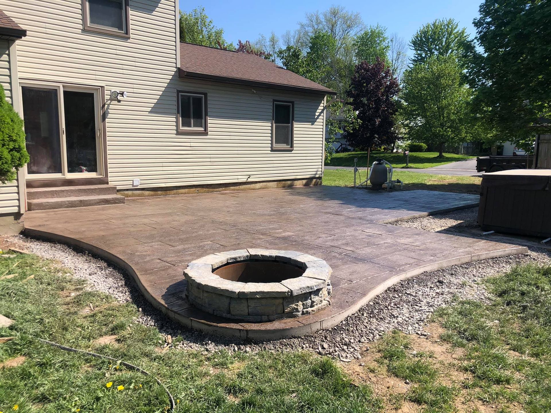 A backyard patio with a fire pit, adjacent to a house with a sliding glass door and a hot tub.