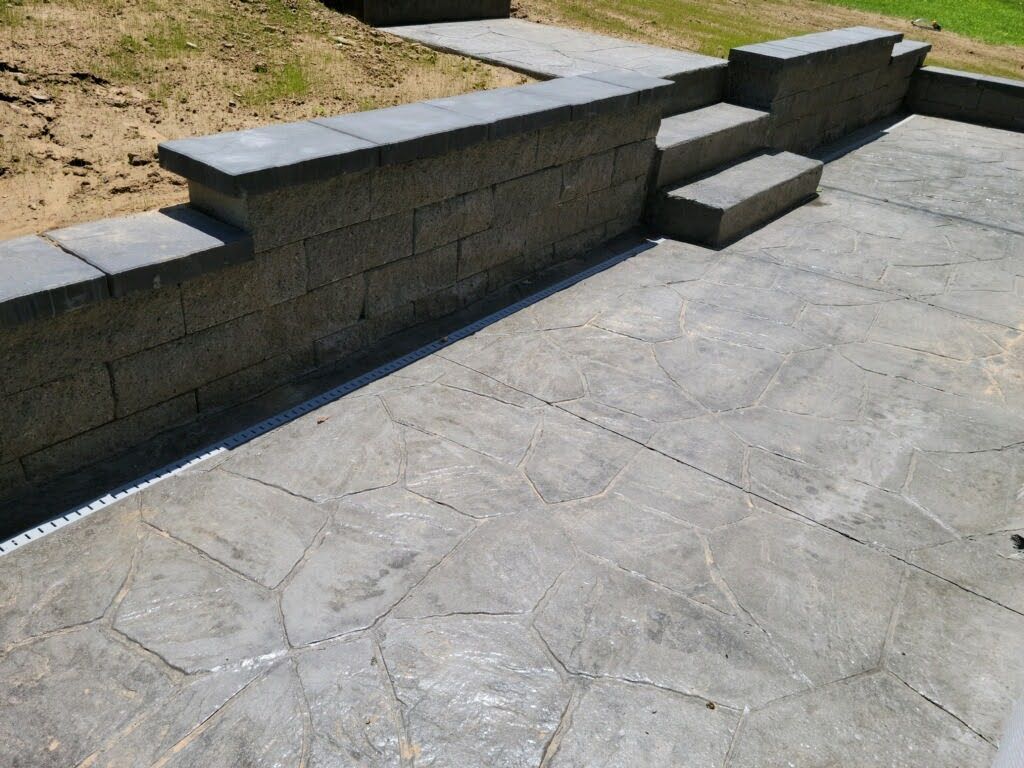 Concrete patio with textured surface, low retaining wall, and steps.