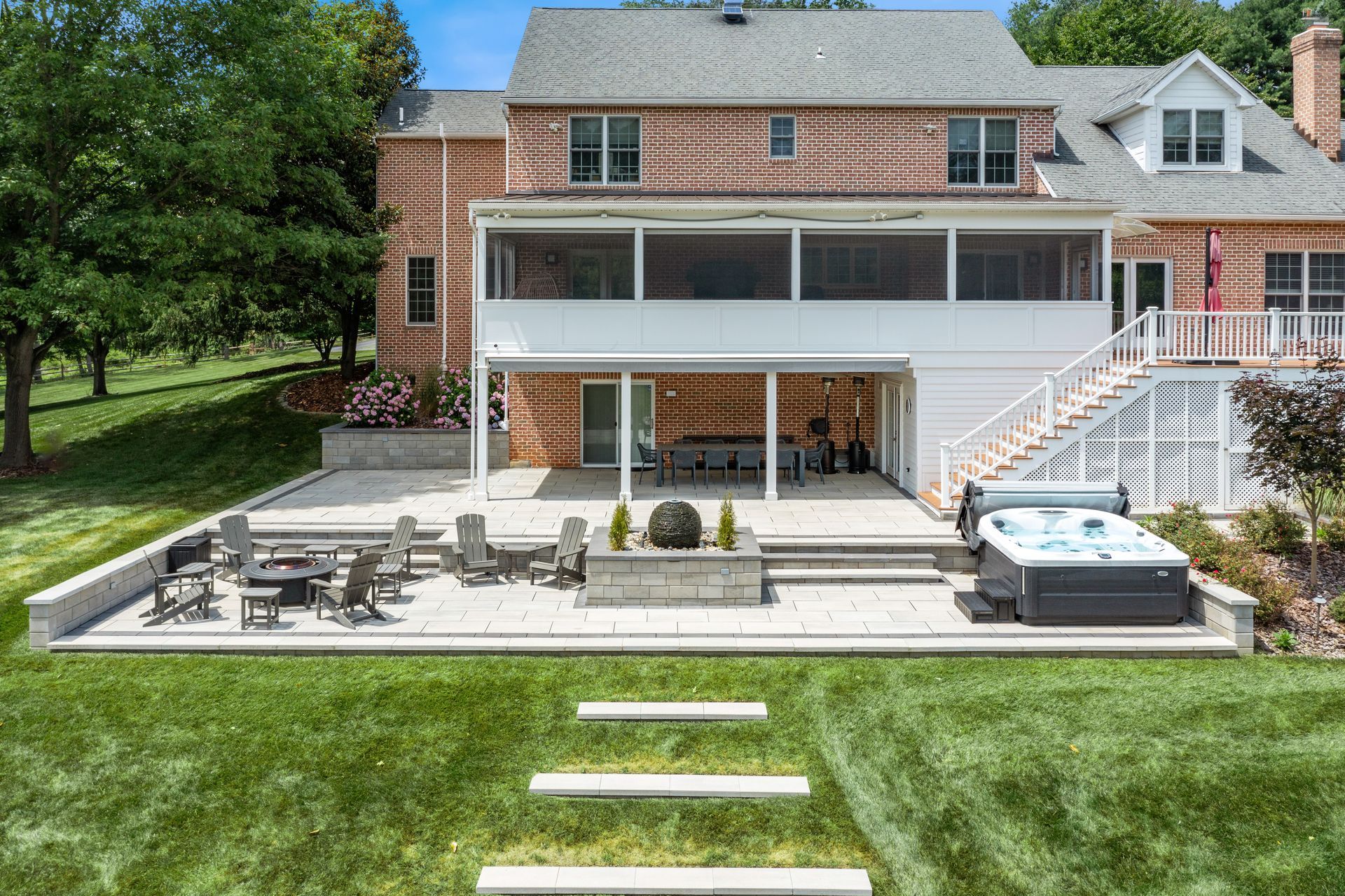Backyard patio with outdoor seating, hot tub, and covered deck beneath a brick house.