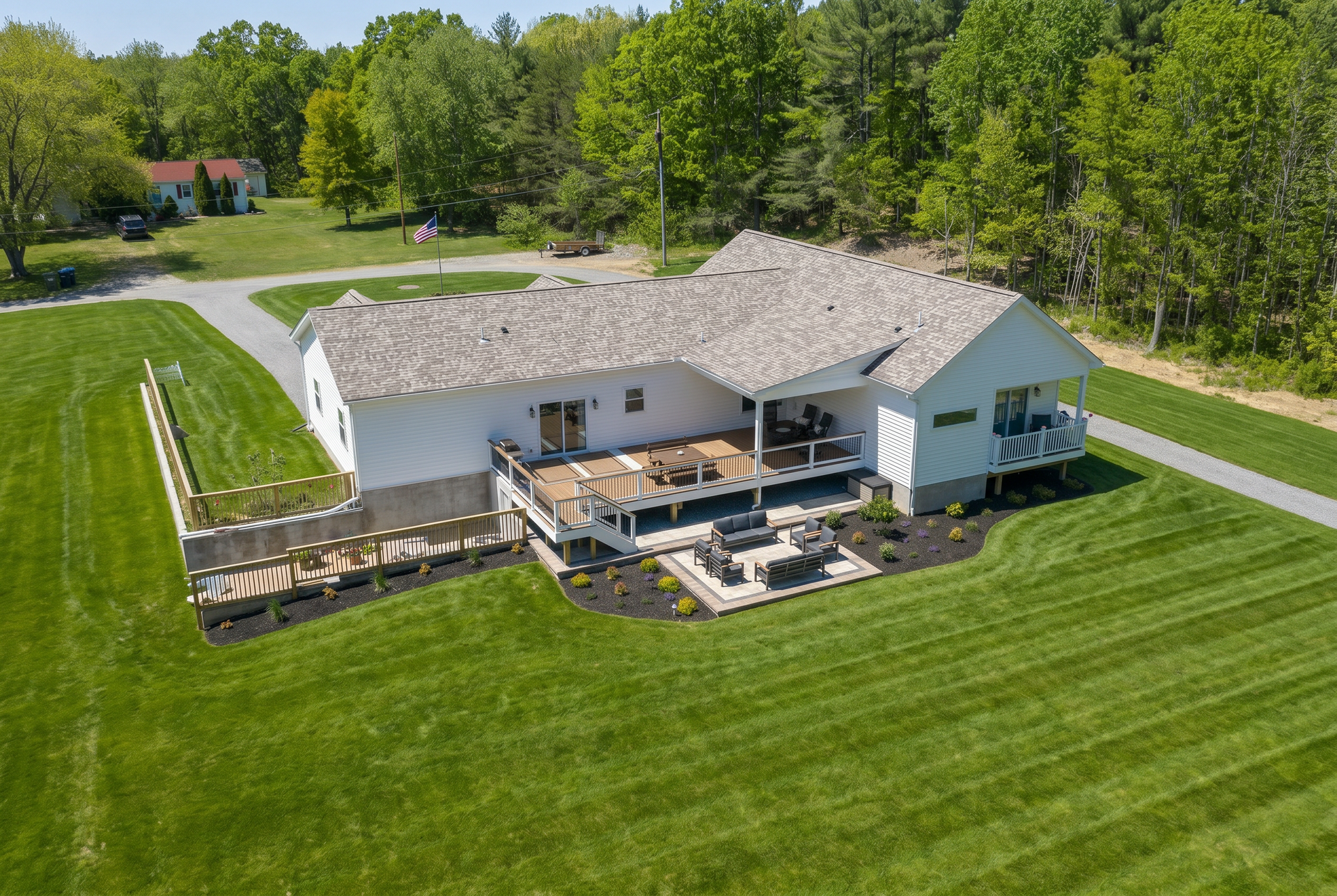 Aerial view of a white house with patio and deck, surrounded by a large green lawn and trees.