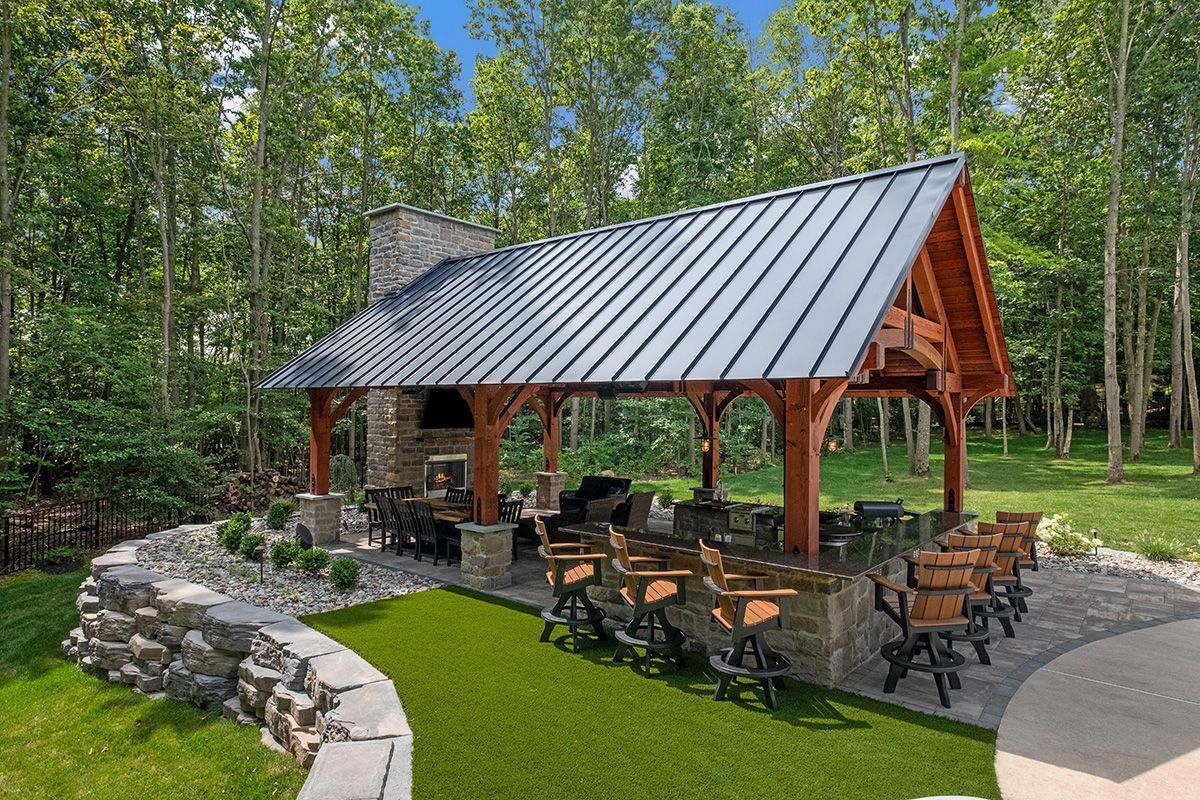 Outdoor pavilion with stone fire pit and metal chairs in a wooded park