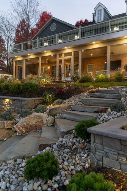 Landscaped stone steps leading to a lit porch on a gray house at dusk