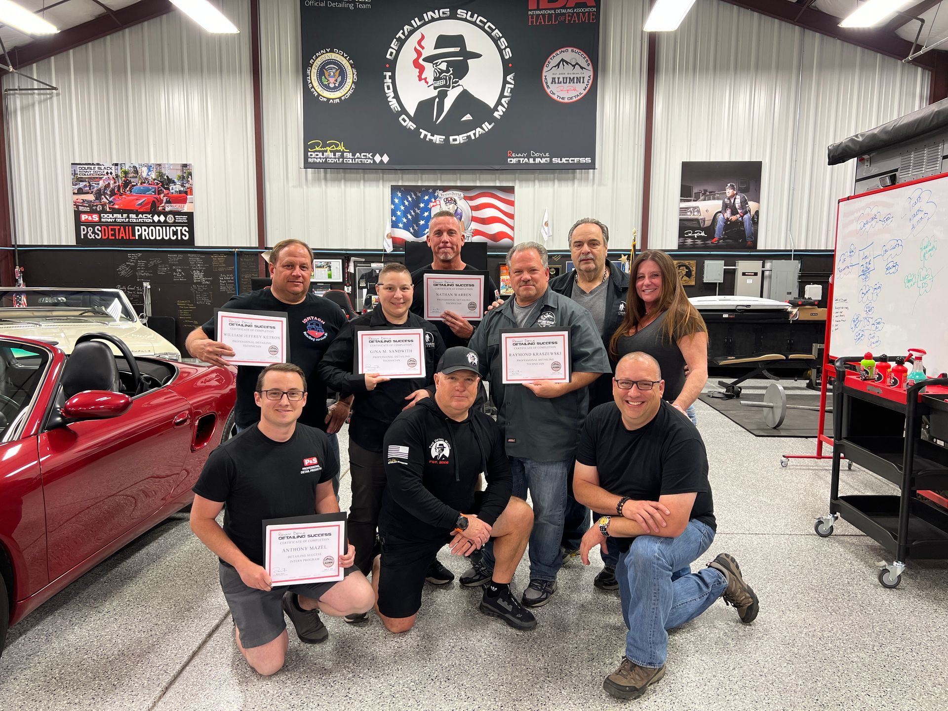 A group of people with certificates, posing in a car detailing shop.