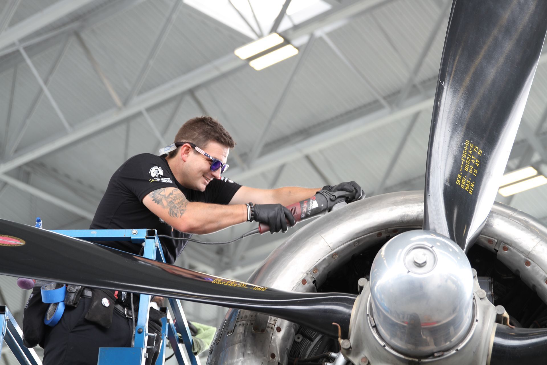 A mechanic wearing safety glasses works on an airplane propeller inside a hangar.