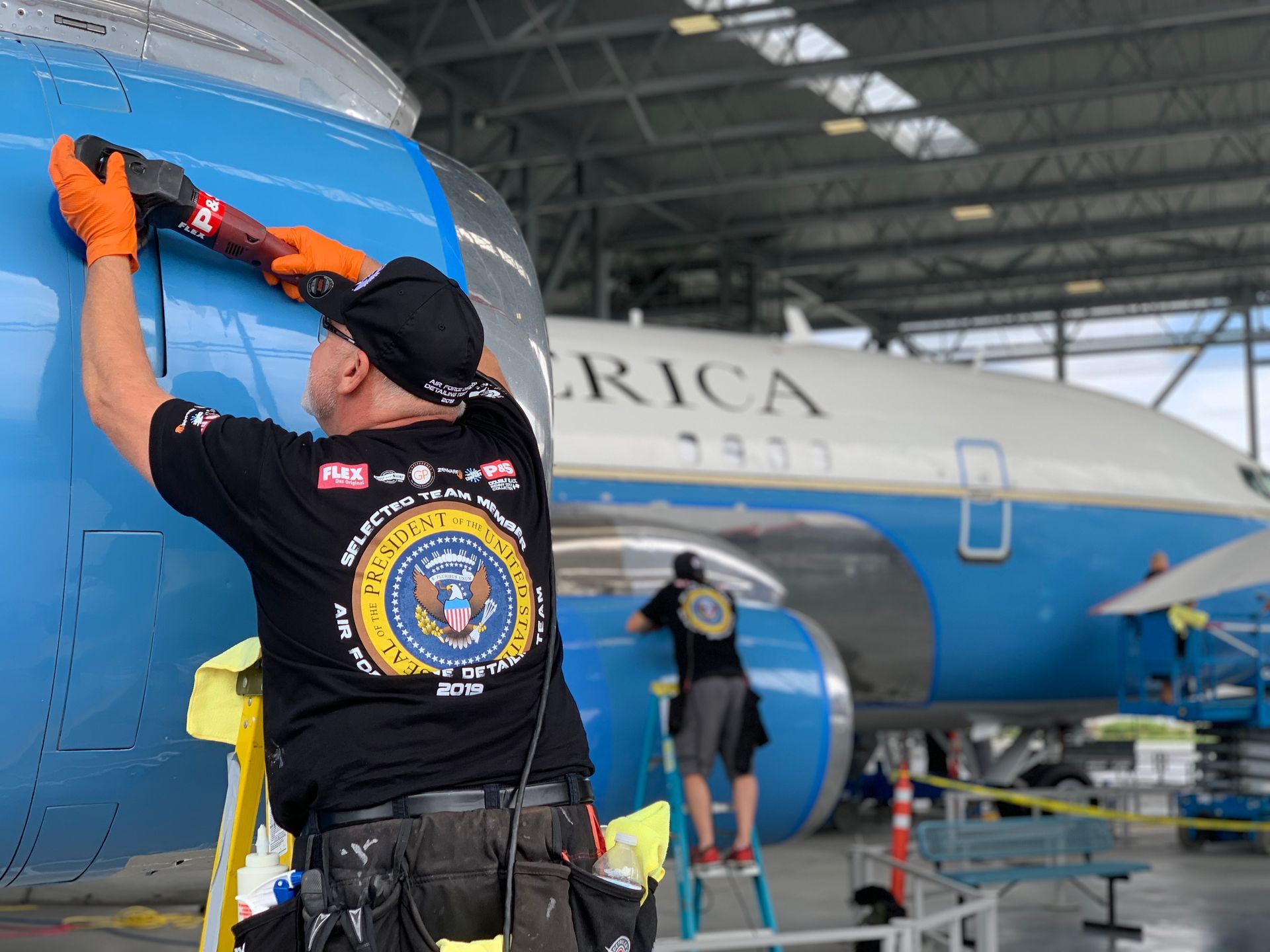 Workers in orange gloves repair a blue and white airplane with
