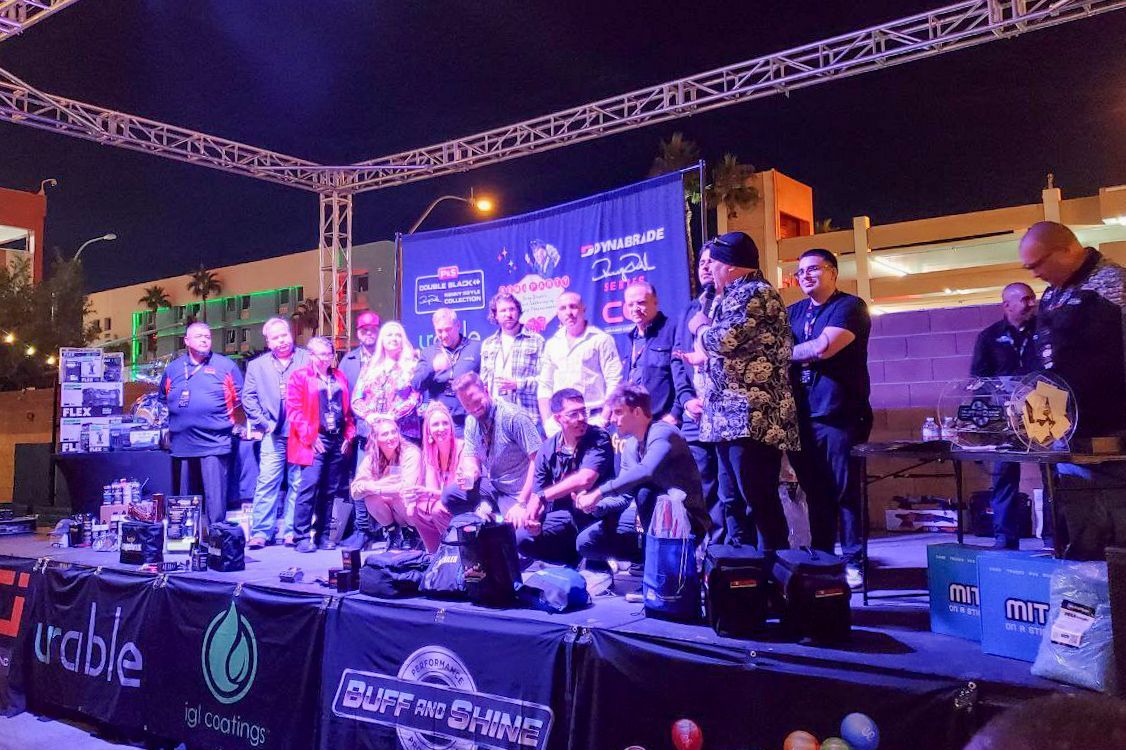 People on stage at night event; banners, lights, and various individuals speaking and listening.