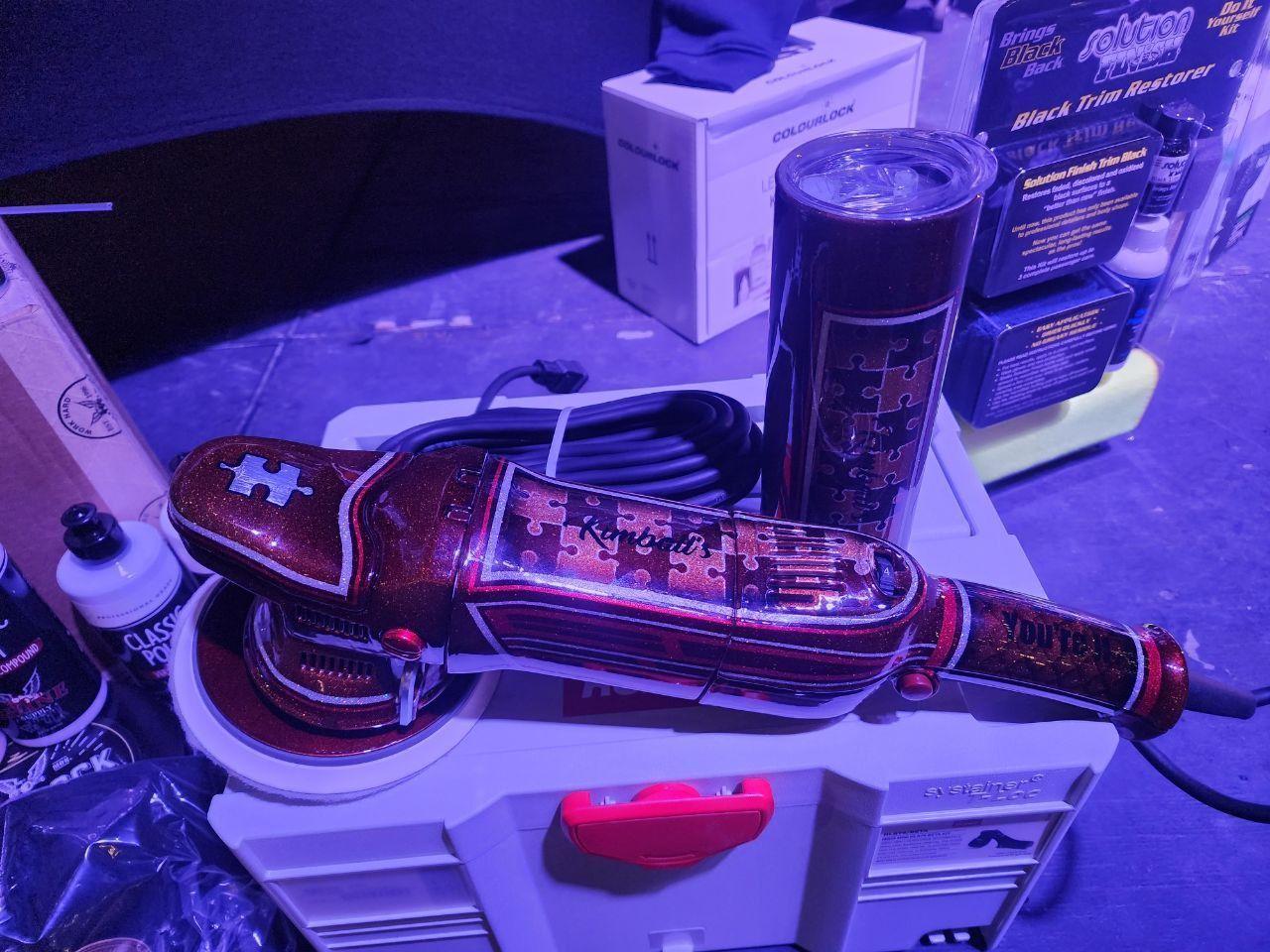 A red and black car polisher and detailing supplies on a workshop bench.