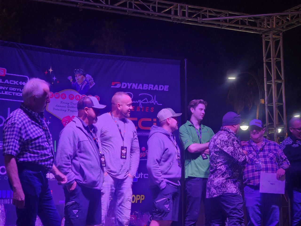 A group of people on a stage under purple lighting. Some are holding certificates.