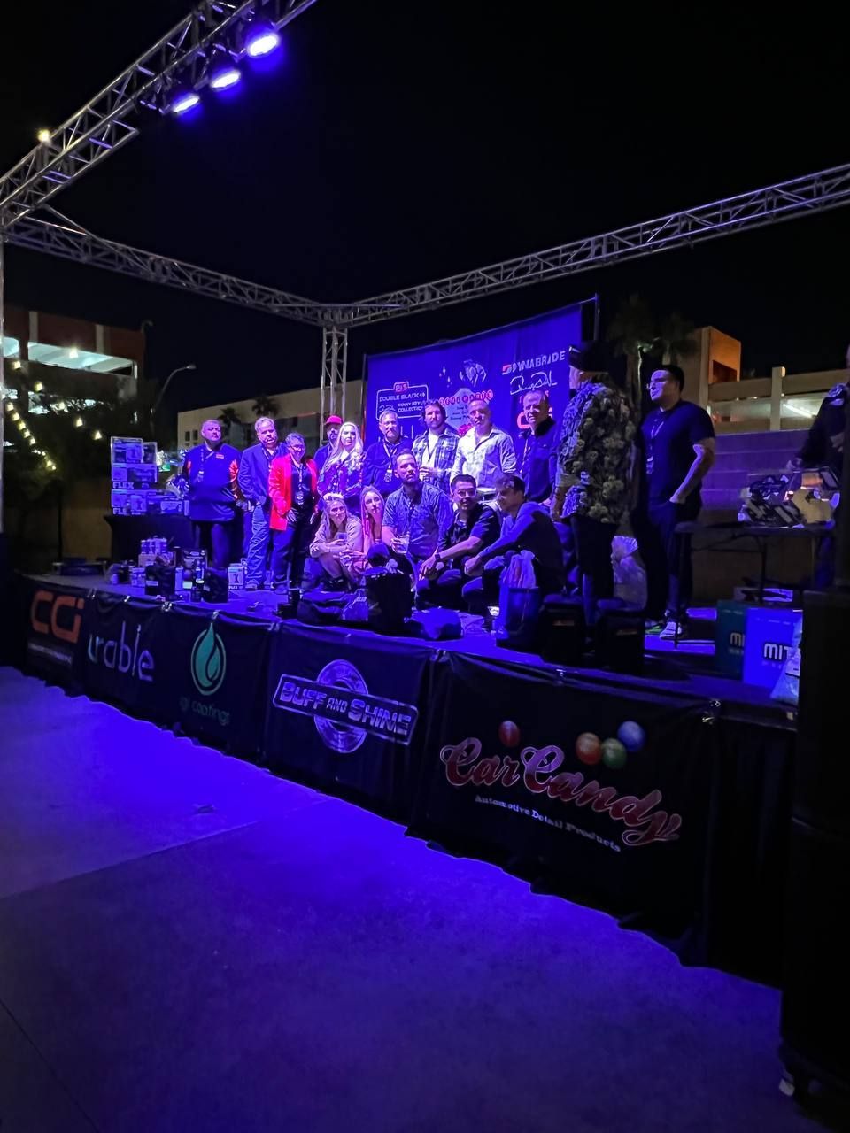 People on stage under lights at night with logos and a dark backdrop.