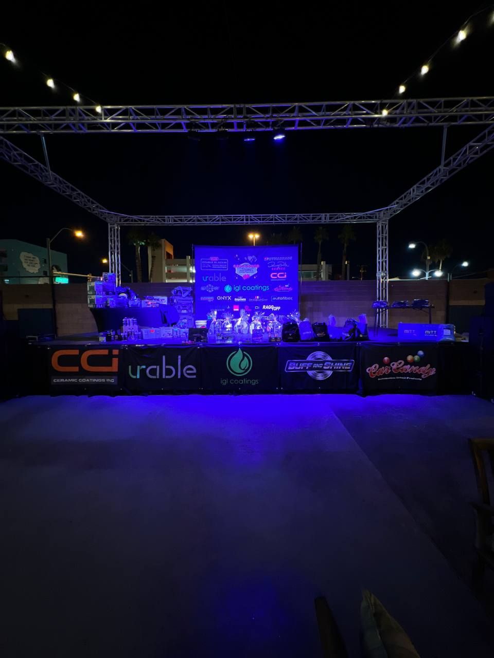 Stage set up for an outdoor event at night, with blue lighting and sponsor logos.