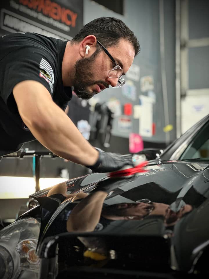 Man wearing glasses and gloves polishing a black car in a garage.